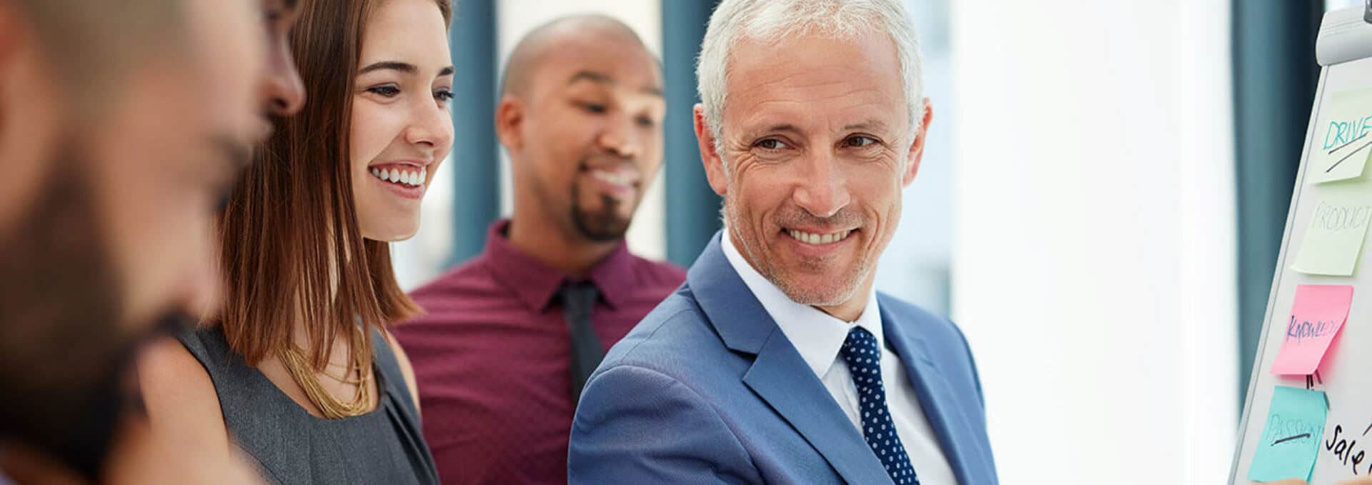 photo of businessman in blue suit smiling while surrounded by coworkers