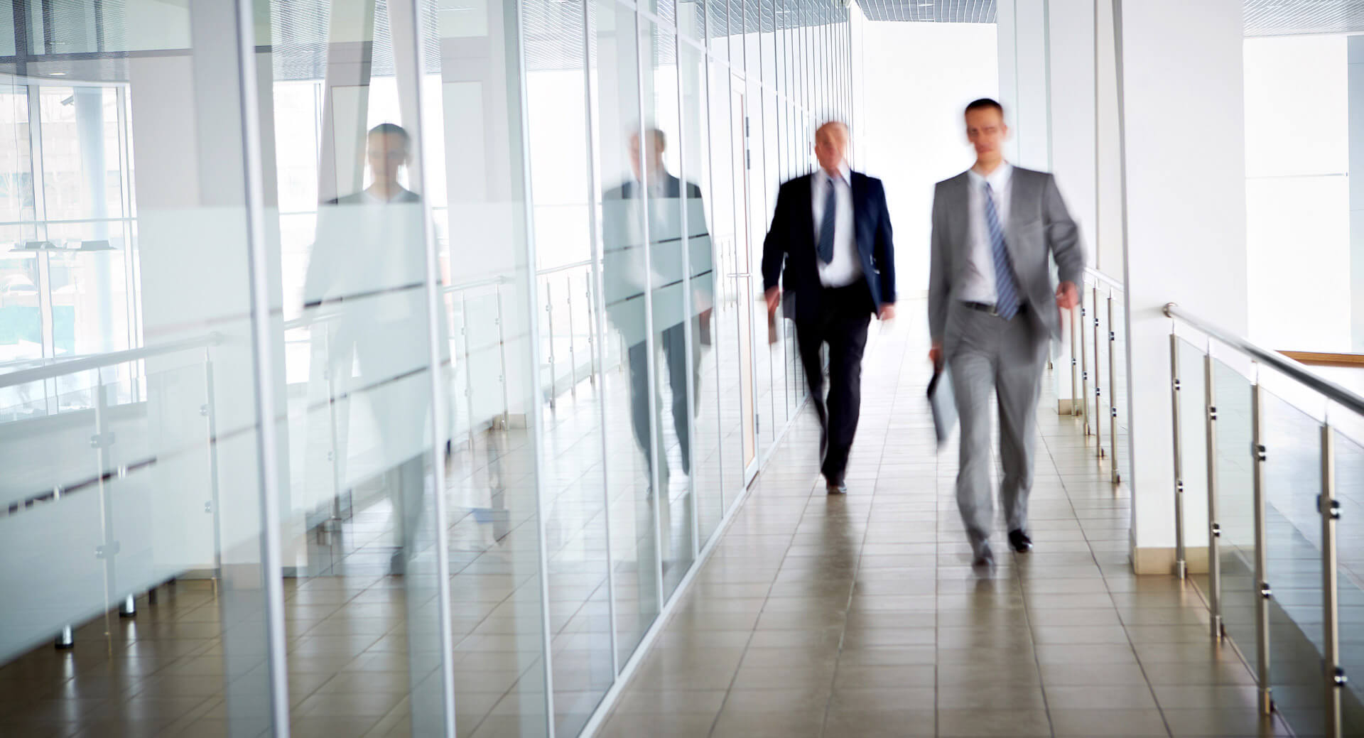 photo of two blurred men in suits walking down office hallway